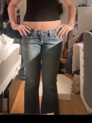 Vintage Blå bootcut jeans från True Religion - Säljer ett par vintage blå bootcut jeans från True Religion med snygga kontrastsömmar och detaljerade bakfickor. Jeansen har låg midja och klassisk femficksdesign. Superfina verkligen men tyvärr för korta för mig! Därför har jag sprättat upp de längst ner, men förutom det är de i väldigt bra skick! De är w28 och jag är ca 176 lång, skulle säga att de är 4-5 cm för korta för mig kanske. Hör av er om ni har frågor! 