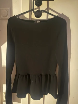 Svart topp med volang från H&M Divided - Säljer en svart långärmad topp från H&M Divided med volang nedtill. Den är i storlek L men jag skulle säga att den passar som storlek S. Använd 2 gånger🌸