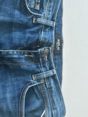 Blå jeans från Replay - Säljer ett par klassiska blå jeans från Replay med snygga kontrastsömmar och femficksmodell. Jeansen har normal midja och är tillverkade i slitstarkt denimtyg. Perfekta för dig som gillar tidlös och avslappnad stil.