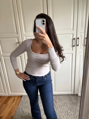 Ljusbeige ribbad långärmad topp - Trendig ljusbeige långärmad topp med ribbad struktur och djup, rundad urringning. Sitter tight och har en stilren, enkel design som passar perfekt till jeans eller kjol.