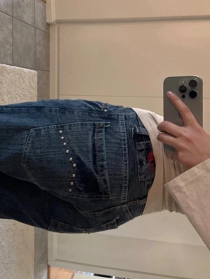 Baggy jeans med nitar på fickan - Säljer ett par baggy jeans i mörkblå denim med coola nitar på bakfickan. Jeansen har en avslappnad passform och klassiska fem fickor. Perfekta för en streetwear-look och passar till det mesta i garderoben.