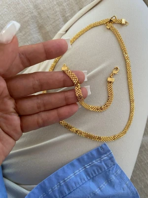Guldfärgat kedjehalsband och armband  guldpläterad  - Säljer ett snyggt halsband i guldfärgad metall med platt, bred kedja och klassiskt lås. Halsbandet har en glansig finish och känns riktigt trendigt och stilrent. Perfekt för att lyfta vilken outfit som helst med en touch av guld.