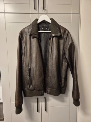Snygg brun skinnjacka i storlek medium  - Snygg brun skinnjacka med ribbade muddar och krage. Jackan har dragkedjeförsedda fickor på sidorna och en klassisk rak passform. Perfekt för dig som vill ha en tidlös och stilren look.