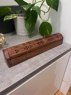 Trälåda för rökelse med stjärnmönster - Säljer en avlång trälåda för rökelsepinnar med utskurna mönster och stjärndekorationer i mässing. Locket har små hål för att släppa ut röken och insidan har plats för flera pinnar. Perfekt för att skapa mysig stämning hemma.