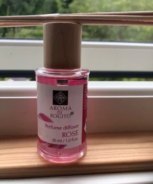 Aroma di Rogito doftdiffuser ros - Helt Ny! Aroma di Rogito doftdiffuser med rosdoft, 30 ml. Flaskan är genomskinlig med rosa vätska och har ett lock i trä. Medföljer doftpinnar i trä för enkel spridning av doften i rummet. Perfekt för att skapa en fräsch och mysig atmosfär hemma.