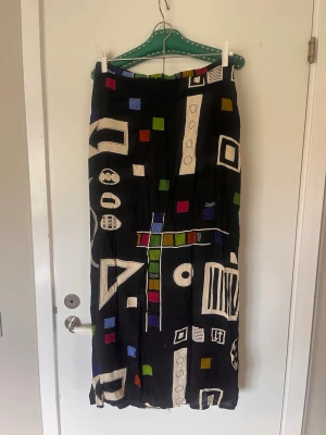 Retrokjol lång cool - Retro kjol 70-tal med coolt mönster. 100 viskos. Lång och rak modell. Dragkedja och knapp baktill. Svart.   Midja 40cm  Stuss 45cm Längd 98cm