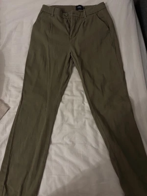 Olivgröna chinos  - Snygga olivgröna chinos från 157 med klassisk rak passform. Byxorna har hällor för bälte, knapp- och dragkedjestängning samt snedställda fickor fram. Perfekta för en stilren och avslappnad look.