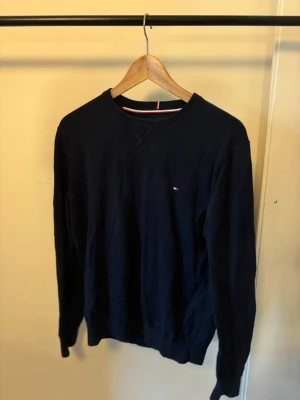 Tommy Hilfiher mörkblå sweatshirt - En stilren mörkblå sweatshirt med rund hals och diskret liten logga på bröstet. Tröjan har långa ärmar och ribbade muddar vid ärmslut och nederkant. Perfekt för en avslappnad och snygg look.