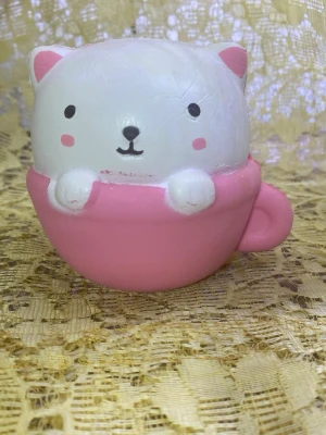 Söt katt squishy i rosa kopp - En mjuk och klämvänlig squishy i form av en vit katt med rosa öron och kinder, sittandes i en rosa kopp. Perfekt som stressleksak eller dekoration. Tillverkad i skumgummimaterial och har en rund, gullig form.