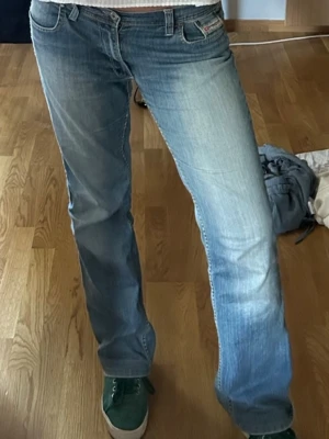 Blå bootcut vintage low waisted jeans från Diesel - Säljer ett par snygga blå bootcut jeans från Diesel med klassisk femficksmodell och slitningar framtill. Jeansen har låg midja och coola detaljer vid fickorna. Köpta på en vintage butik i Amsterdam. Är 177cm låg och de går ner till fötterna på mig.