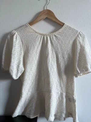 Vit spetsblus från Holly & White - Söt vit blus från Holly & Whyte by Lindex i spetsmaterial med puffiga korta ärmar och rund halsringning. Blusen har fina virkade detaljer vid halsen och ett lätt utställt avslut. Den har en liten fläck (sista bilden) , men den syns knappt.