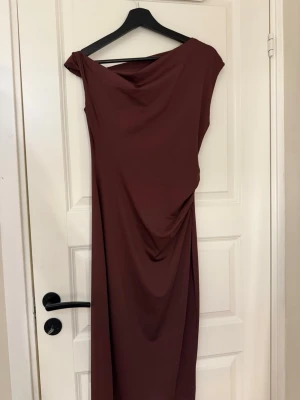 Asymmetrisk vinröd midiklänning - Säljer en vinröd, midilång klänning med asymmetrisk axel och draperad detalj i sidan från Zara. Klänningen har en elegant, figurnära passform och är tillverkad i ett mjukt, stretchigt material. Perfekt för dig som vill ha en unik och stilren look. Har bara använt den 1 gång.