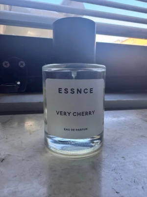 ESSNCE Very Cherry Eau de Parfum - ESSNCE Very Cherry Eau de Parfum i en stilren, genomskinlig glasflaska med svart lock. Doften har en fräsch och söt körsbärston. Flaskan har en enkel vit etikett med svart text och känns modern och minimalistisk.