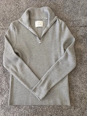 Grå ribbstickad tröja Jack & Jones - Snygg grå ribbstickad tröja från Jack & Jones med halv dragkedja och hög krage. Tröjan har långa ärmar och är tillverkad i ett mjukt, stretchigt material som passar perfekt till vardagslooken.