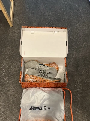 Nike Mercurial Superfly 10 Elite FG - Säljer ett par Nike Mercurial Superfly 10 Elite FG fotbollsskor i orange med svartprickigt mönster och grå ovandel. Skorna har strumpliknande skaft och är designade för spel på fasta underlag. Medföljer originalpåse och låda.