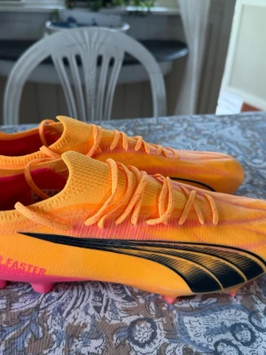 Puma orangea fotbollsskor elite - Säljer ett par grymma orangea fotbollsskor från Puma med svart logga på sidan. Skorna har snörning, låg profil och är tillverkade i ett lätt syntetmaterial. Sulan har dobbar i rosa för bra grepp på planen. Perfekta för dig som vill sticka ut på matchen! Ny pris 2700 kr 