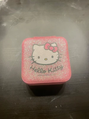 Hello Kitty smyckesask rosa glitter - Söt rosa smyckesask med glitter och Hello Kitty-motiv på locket. Insidan har flera fack och ringrullar samt en hjärtformad spegel. Perfekt för att organisera smycken och accessoarer.