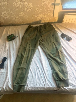  Nike mjukisbyxor - Säljer ett par olivgröna mjukisbyxor från Nike med dragsko i midjan och ribbade muddar vid bensluten. Byxorna har en avslappnad passform och är tillverkade i mjukt bomullsmaterial. Nike-logga i blått på vänster lår. Perfekta för chill dagar. Kan gå ner något i pris vid en riktigt snabb och smidig affär! 