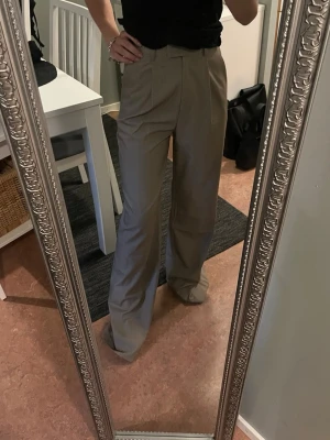 Beiga vida kostymbyxor Djerf Avenue  - Säljer ett par beiga (greige) kostymbyxor (favourite pants oat tall) med hög midja och vida ben. Byxorna har pressveck framtill och stängs med dragkedja och hake. Perfekta för en clean och stilren look. Från djerf avenue nya med prislapp!  
