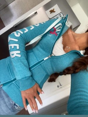 Turkos tajt zipup hoodie från Hollister - Gullig ljus turkos blå zip hoodie från Hollister i strl M (omsydd till xxs) med logan broderat längs armen💓 följ för fler liknande zipups!