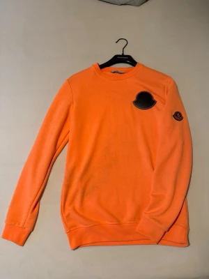 Orange sweatshirt med svart patch - Cool orange sweatshirt med rund hals och stora svarta patches på bröstet och ärmen. Tröjan har en avslappnad passform och ribbade muddar vid ärmslut och nederkant. Perfekt för dig som vill sticka ut med färg och enkel design.
