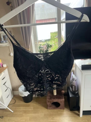 Svart spetsbralette med smala band - Säljer en svart bralette i genombruten spets med smala axelband och vacker blommig spetsdetalj. Braletten har en längre modell som går ner över bröstkorgen och ger en trendig look. Perfekt för dig som gillar mjuka och bekväma underkläder med snygg design.
