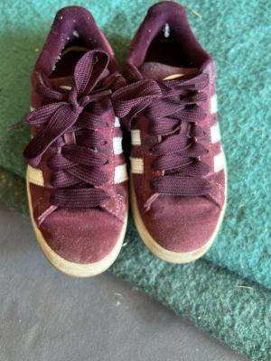 Vinröda Adidas Campus sneakers mocka - Säljer ett par vinröda Adidas Campus sneakers i mocka med klassiska vita ränder på sidorna och breda snören. Gott skick 7/10. Dm vid frågor. 