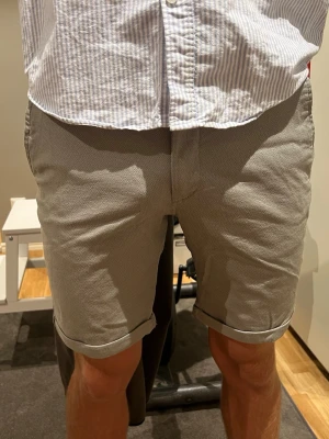 Beige shorts med uppvikta ben - SKJORTSEN HAR ALDRIG ANVÄNTS.. PRISLAPP KVAR. .Snygga beige/gröna shorts med uppvikta ben och klassisk passform. De har knapp och dragkedja framtill samt bälteshällor i midjan. Perfekta för varma dagar och enkla att matcha med olika stilar. 