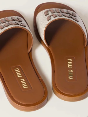 Beige sandaler från Miu Miu - Stilrena sandaler från Miu Miu i beige textil med bred rem och broderad logga i brunt. Sulan är i brunt läderliknande material och har en platt design. Perfekta för en avslappnad och trendig look. Storlek 41 men passar mig som har 40