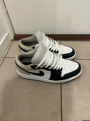 Svarta och vita låga sneakers - Snygga låga sneakers i svart och vitt med beige detaljer. Skorna har klassisk siluett, perforerad tåbox och vita skosnören. Tillverkade i läder med vadderad häl och sula i gummi. Perfekta för dig som gillar stilrena och sportiga sneakers.