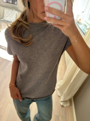 Grå basic t-shirt i mjukt material - En enkel grå t-shirt med rund hals och korta ärmar. Tillverkad i ett mjukt, stretchigt material som sitter skönt på kroppen. Perfekt att matcha med jeans eller kjol för en avslappnad look.