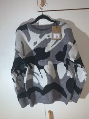 M. Camo grå stickad - Köpte den va för lite på mig tänkte ville ha lite tight fit har L i verkligheten modellen är redan bra fit Säljer en stickad tröja i olika nyanser av grått, svart och vitt med ett coolt abstrakt mönster. Tröjan har rund halsringning, långa ärmar och ribbade muddar vid ärmslut och nederkant. Perfekt för dig som gillar unik design och sköna material.