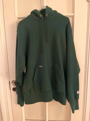 Palace Mörkgrön hoodie med ficka och huva - Snygg mörkgrön hoodie från palace med stor känguruficka framtill och justerbar huva med snören. Hoodien har ribbade muddar vid ärmslut och nederkant samt en liten diskret logga på fickan. Perfekt för en avslappnad och chill stil.