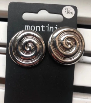 Silvriga spiralörhängen Montini - Säljer ett par coola örhängen från Montini i blankt silverfärgat material. De är runda med ett spiralformat mönster som ger en unik och trendig look. Perfekta för dig som vill sticka ut med dina accessoarer.