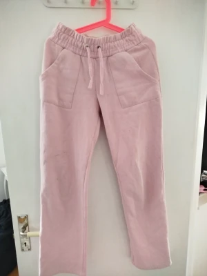 Ljusrosa mjukisbyxor med raka ben - Säljer ett par ljusrosa mjukisbyxor med raka ben och resår i midjan. Byxorna har snörning i midjan, två stora fickor fram och två bakfickor. Perfekta för chill dagar hemma eller när du vill vara bekväm. Materialet känns mjukt och skönt mot huden.