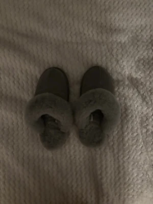Grå fluffiga tofflor i mocka - Mysiga grå tofflor med fluffig päls runt öppningen och ovansida i mocka. Perfekta att glida runt i hemma när det är kallt. Klassisk slip-in modell med hård sula och stilren look.
