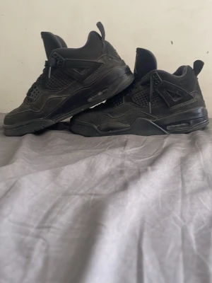 Joarden 4 black cats - Säljer ett par helsvarta sneakers med högt skaft och meshdetaljer på sidorna. Skorna har snörning, vadderad plös med logga och synlig luftdämpning i sulan. Perfekta för dig som gillar en sportig och clean look. Strl 40 men passar dig som är eur 39 