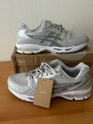 ASICS GEL-KAYANO 14 – Helt nya – Silver/Vit – Originalkartong - Säljer ett par helt nya ASICS GEL-KAYANO 14 i den stilrena silver/vita färgen. Skorna är oanvända och levereras i originalkartong.  GEL-KAYANO 14 är en populär modell som kombinerar en klassisk Y2K-design med modern komfort. De passar lika bra till vardags som för promenader och ger utmärkt dämpning och stabilitet tack vare ASICS GEL-teknologi. Den ventilerande mesh-ovandelen ger en bekväm känsla hela dagen.