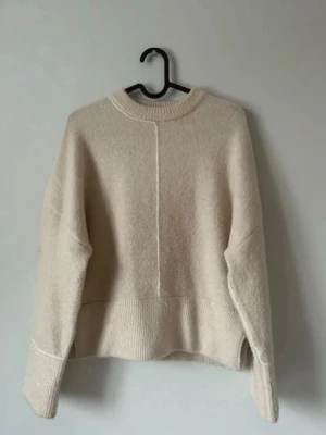 Zara stickad tröja - Mysig beige stickad tröja i oversize-modell med rund halsringning och ribbade muddar. Tröjan har en dekorativ söm framtill och är tillverkad i ett mjukt material som passar perfekt för kyligare dagar.