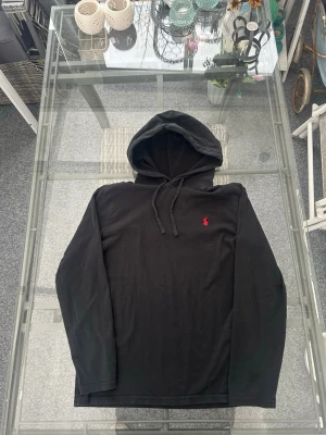 Polo Ralph Lauren svart hoodie med röd logga – Strl S – Original & fint skick - Svart hoodie från Polo Ralph Lauren i mycket bra skick. Klassisk modell med röd broderad logga på bröstet. Stilren, bekväm och lätt att matcha med alla outfits.  ✔️ Original ✔️ Färg: Svart / röd logga ✔️ Storlek: S (Small) ✔️ Material: 100% bomull ✔️ Skick: Mycket fint, sparsamt använd ✔️ Passform: Regular fit  Perfekt för vardag, skola, streetwear eller chill outfits. Funkar året runt och passar både casual och trendig stil.