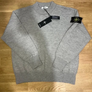 Stone Island Tröja - Stickad tröja från Stone Island i klassisk ljusgrå färg. Rund hals, ribbade muddar och nederkant samt den ikoniska Stone Island-badgen på ärmen. Storlek M med normal passform. Helt ny, aldrig använd. Originaltags medföljer. Skickas snabbt och säkert vid affär. Det går o diskutera priset🤍. Skriv vid frågor eller intresse.😊