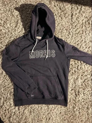  Mörkblå hoodie från Morris🙌 - Snygg svart hoodie från Morris med vit broderad logga på bröstet och vita dragsnören i huvan. Klassisk känguruficka framtill och ribbade muddar vid ärmslut och nederkant. Perfekt för en avslappnad och trendig stil.🙌🤩