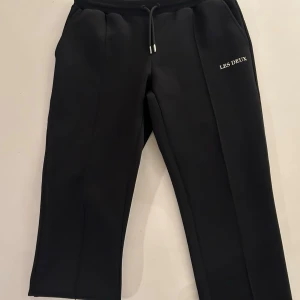 Svarta mjukisbyxor från Les Deux - Snygga svarta mjukisbyxor från Les Deux med diskret logga på vänster sida. Byxorna har dragsko i midjan och raka ben. Tillverkade i ett mjukt och stretchigt material som ger en avslappnad och modern look.