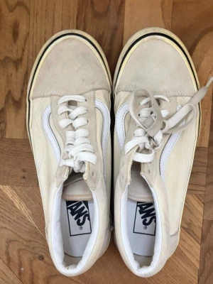 Beige Vans Old Skool sneakers - Snygga beige Vans Old Skool sneakers med klassisk vit sidorand och vita snören. Ovandelen är i mocka och canvas, med en retroinspirerad sula i offwhite. Perfekta för en avslappnad streetstyle-look.