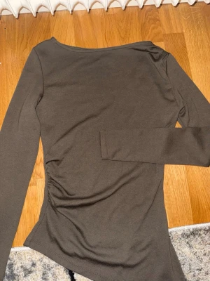 Långärmad topp med rynk - Säljer en enkel och stilren olivgrön långärmad topp med rynkdetalj på sidan. Toppen har en mjuk och stretchig känsla, perfekt för att matcha med jeans eller kjol. Materialet känns som bomull eller en bomullsblandning och modellen är figurnära.