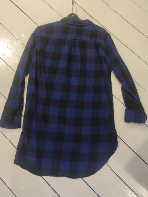 Blårutig långärmad skjorta - Snygg blårutig skjorta med svart rutmönster och klassisk krage. Skjortan har långa ärmar, knappar framtill och en avslappnad passform. Perfekt att bära öppen eller stängd för en chill look.