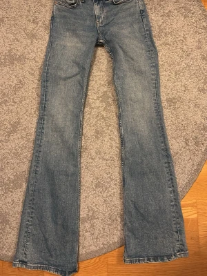 Blå bootcut jeans från Gina Tricot - Säljer ett par klassiska blå bootcut jeans från Gina Tricot. Jeansen har fem fickor, låg/normalhög midja och lätt utsvängda ben. Tillverkade i denim med en snygg tvättad look och detaljerade sömmar. Perfekta för dig som gillar retrostil. Nypris är 399