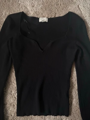 Svart ribbad långärmad topp Gina Tricot - Snygg svart ribbad topp från Gina Tricot med lång ärm och v-ringad halsringning. Modellen är tight och har en croppad passform som passar perfekt till höga jeans eller kjol. Enkel men trendig design som är lätt att styla.