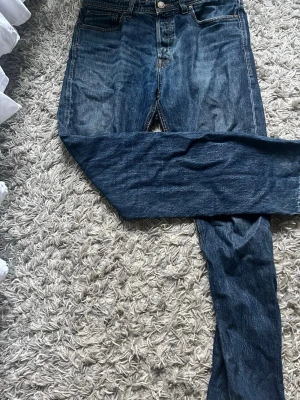 Blå jeans från Jack & Jones - Säljer ett par klassiska blå jeans från Jack & Jones med fem fickor och knappgylf. Jeansen har en snygg tvättad look och raka ben. Perfekta till en avslappnad stil och tillverkade i slitstarkt denimtyg.