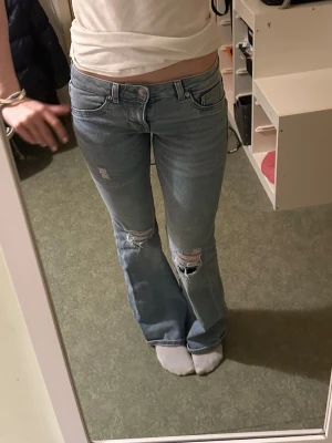 Ljusblå bootcut jeans med slitningar - Säljer ett par ljusblå bootcut jeans med slitningar och hål vid knäna. Jeansen har klassisk femficksmodell, låg midja och dragkedja med knapp. Jag är 168 cm för referens💕